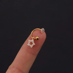 Dettaglio di un piercing barbell dorato con pendente a stella e pietre di zircone cubico