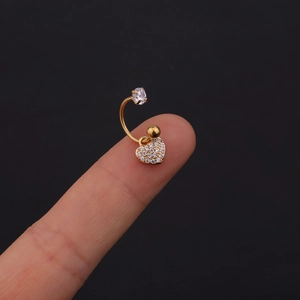 Dettaglio di un piercing all'ombelico dorato con ciondolo a cuore in zirconi pavé