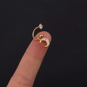 Dettaglio macro di un piercing a C dorato con mezzaluna e zirconi tenuto sulla punta del dito