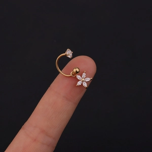 Dettaglio macro di un orecchino a C dorato con pendente a fiore in zircone su dito