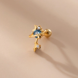 Dettaglio del piercing a chiave dorata con zircone blu e motivi di stelle e luna sulla banda