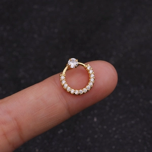 Macro shot of a golden piercing ring with white cubic zirconia stones on a fingertip