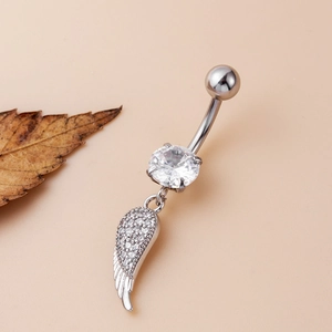 Piercing de ombligo de acero con colgante de ala de ángel y circonitas sobre fondo rosa