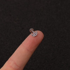 Macro shot of a tiny stainless steel crown earring with white zircons on a fingertip