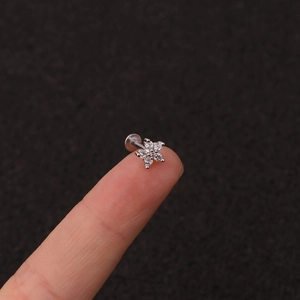 Macro shot of a tiny silver crown stud earring with five clear zircons on a fingertip