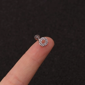 Macro shot of a small crown crystal stud earring held on a fingertip for size scale
