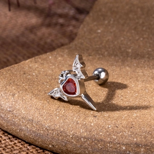 Macro del piercing cartilagine gotico con ali di pipistrello e zircone rosso a cuore
