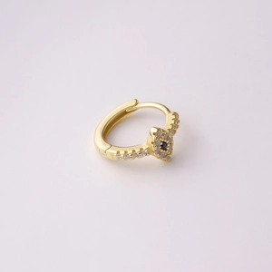 Detail of gold huggie earring with blue zircon eye and pavé crystals on pink background