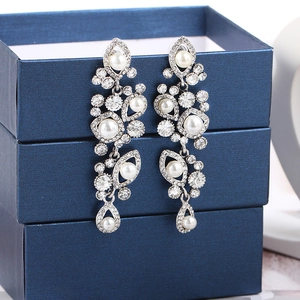 Macro detail of silver drop earrings featuring crystal clusters and white pearls on blue base