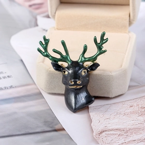 Detail of stag head brooch with black enamel and green antlers on beige velvet box