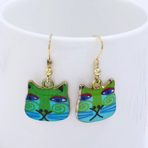Artistic cat drop earrings with blue and green enamel hanging on a white ceramic cup