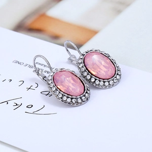 Macro detail of oval pink gemstone earrings with white zircon halo on a clean white background