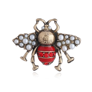 Vintage gold bee brooch with white pearl wings and red crystal accents on white background