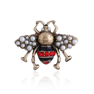 Detailed close-up of a vintage bee brooch with white pearls and red rhinestones