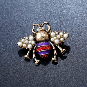Macro view of vintage bee brooch featuring pearl wings and purple enamel body with red rhinestones
