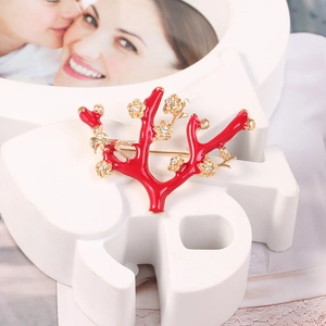 Detail of red coral brooch with gold flowers and crystals on a white pedestal