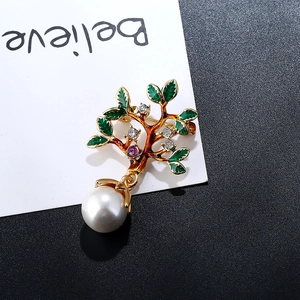 Détail d'une broche arbre dorée avec feuilles vertes et une grande perle blanche pendante