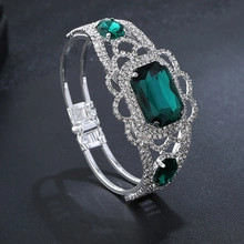 Detail van zilverkleurige armband met smaragdgroene stenen en pavé gezette kristallen