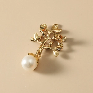 Broche branche dorée avec une grande perle blanche sur un fond beige clair