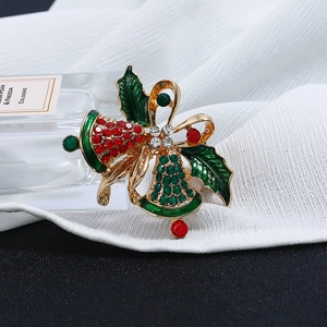 Close-up of Christmas bow bell brooch with red and green rhinestones on white fabric