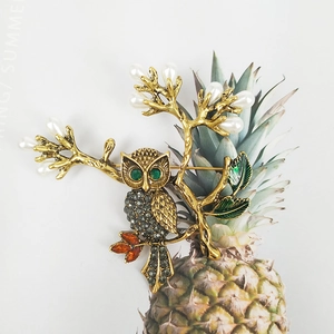 Macro detail of owl brooch with green rhinestone eyes and white pearls on gold branch
