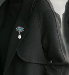Macro detail of retro evil eye brooch with blue stone and pearl on a coat lapel