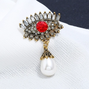 Macro shot of evil eye brooch featuring a red crystal, clear rhinestones, and drop pearl