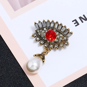 Macro shot of retro Evil Eye brooch featuring red crystal, rhinestones and pearl drop