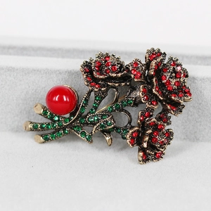 Detailed macro of vintage rose brooch with red crystals and green leaves on velvet