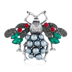 Detail of vintage silver insect brooch with red crystals, green gems and a large faux pearl