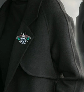 Detailed close-up of a bee brooch with red and green crystals on a black wool coat