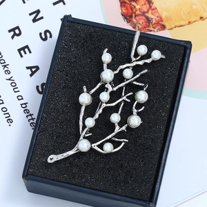 Détail de la broche branche argentée avec perles blanches dans un écrin bleu