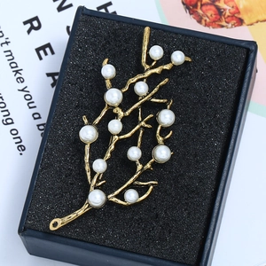 Détail d'une broche branche vintage dorée avec perles blanches dans son écrin
