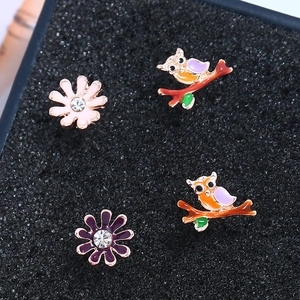 Macro shot of owl enamel studs and floral earrings with zircons on black sponge