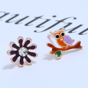 Macro shot of asymmetric owl and purple flower earrings with enamel and rhinestone details