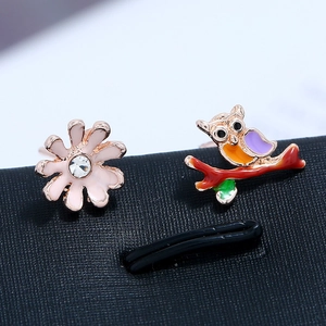 Macro detail of asymmetric owl and flower stud earrings with colorful enamel coating