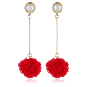Detail showing long drop earrings with white pearls and bright red furry pom-pom pendants