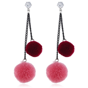 Detail of long asymmetric earrings with plush poms, metal chains, and sparkling rhinestones