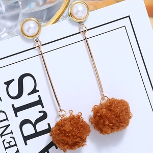 Detailed shot of long gold earrings featuring white pearls and brown fluffy pom-poms