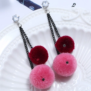 Detailed view of long plush ball earrings with rhinestones on a white ceramic plate