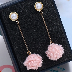 Detail of pink faux fur pompom earrings with white pearls on a black jewelry cushion