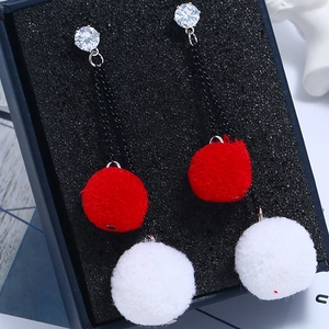 Detail of long plush earrings with red and white balls in a dark blue gift jewelry box