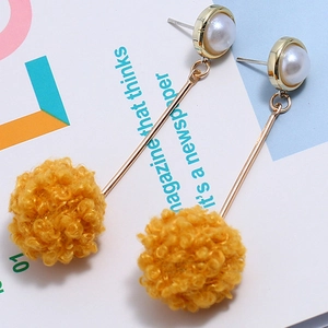 Long drop earrings featuring white pearls and yellow pom pom balls on a fashion magazine