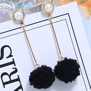 Detail view of long dangle earrings with white pearl, gold rod, and black faux fur pom poms
