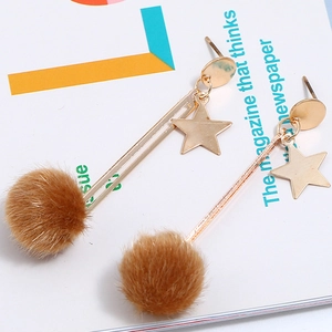 Detail view of long gold earrings featuring star charms and brown faux fur pom poms