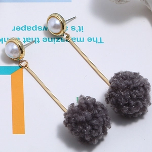 Detail view of long drop earrings with white pearls and grey fluffy pom-poms on gold stems