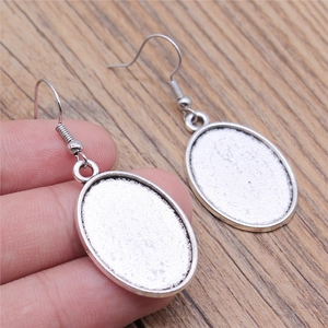 Silver oval leverback earrings with textured glitter finish held in hand over wood surface