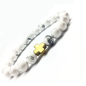 Yoga-Armband aus weißen Türkisperlen mit poliertem goldenem Metallkreuz auf weißem Hintergrund