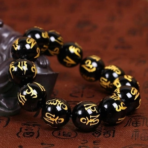 Dettaglio macro di perle di cristallo nero lucido con mantra dorato per bracciale spirituale