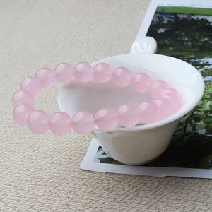 Close-up of polished pink rose quartz beaded bracelet hanging on a white ceramic cup